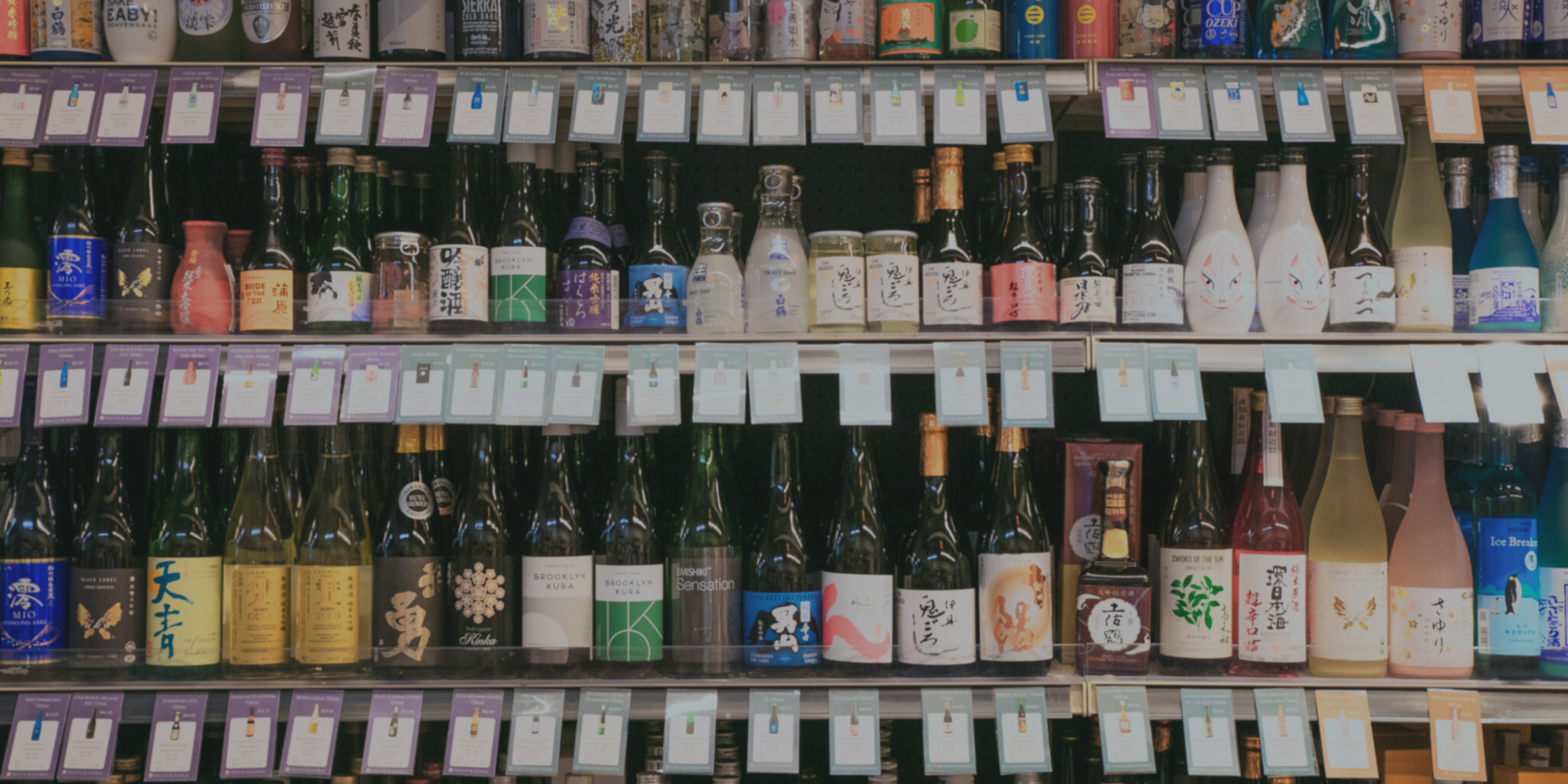 Shelves of various bottles of sake and Japanese spirits with labels and price tags in a store.